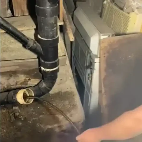 Drain cable fed into an open sewer cleanout on a black drain stack before cleaning