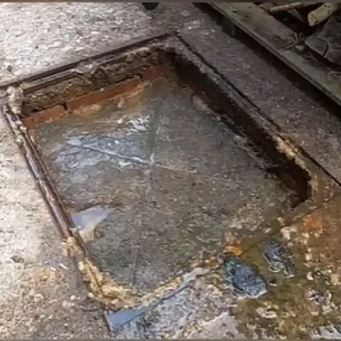 Brick-lined floor drain full of standing water and greasy buildup before cleaning