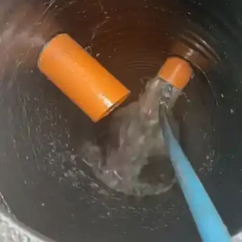 Round drain basin with water flowing from a blue hose after clearing a clogged drain
